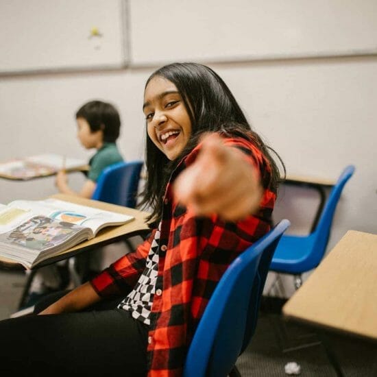 girl sitting on her desk while pointing towards the camera