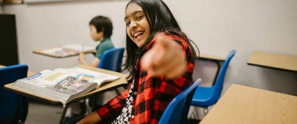 girl sitting on her desk while pointing towards the camera