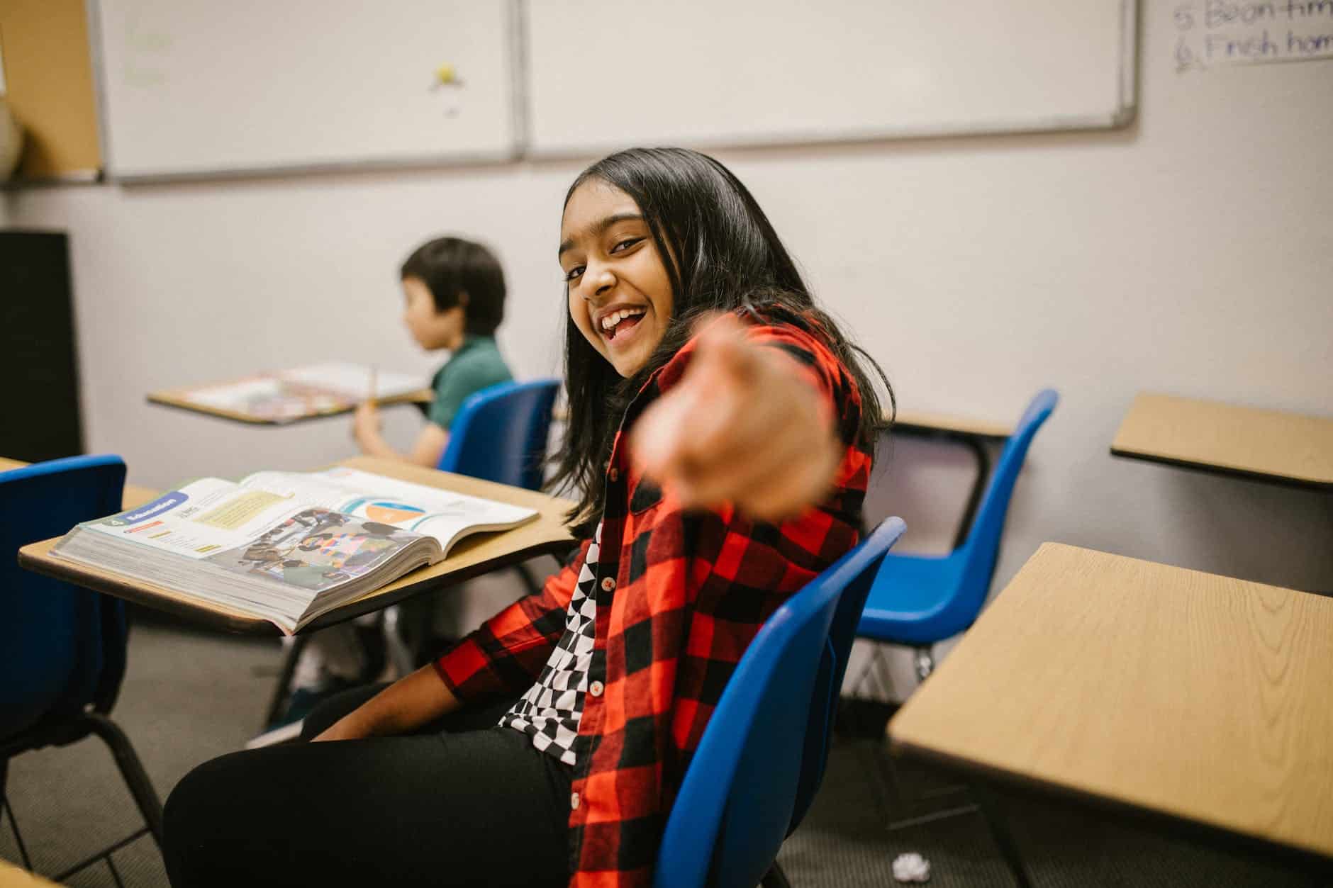girl sitting on her desk while pointing towards the camera