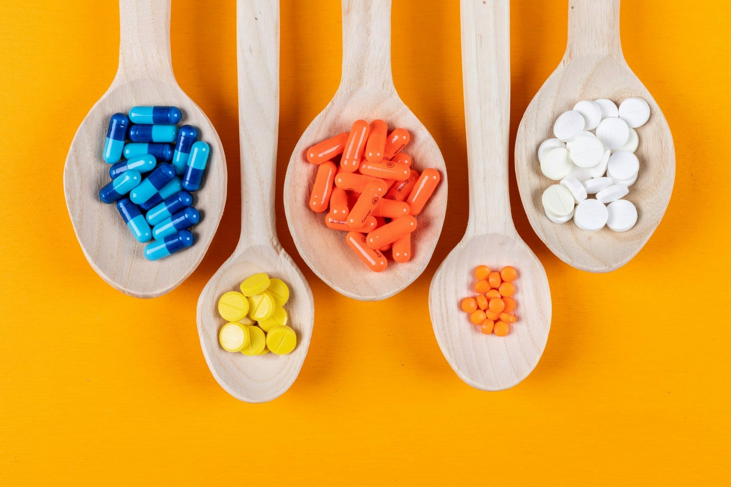 Top view colorful pills in wooden spoons on orange background. horizontal
