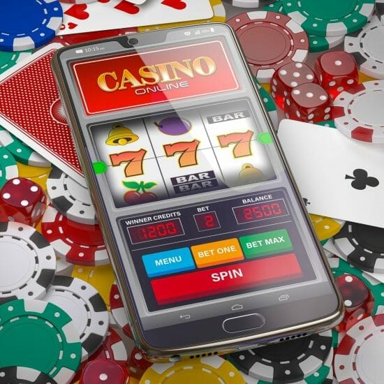 Online casino. Slot machine on smartphone screen, dice, casino chips and cards.