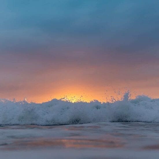 sunset sky over waving sea washing shore