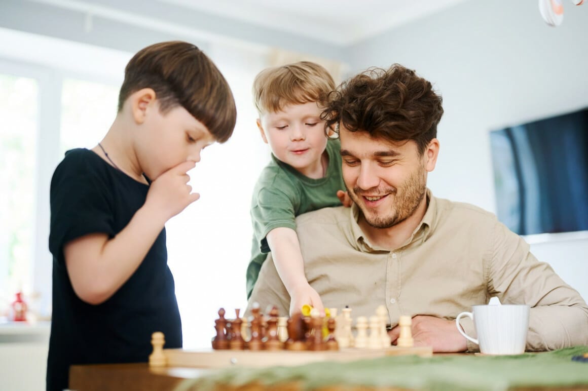 father teaching sons how play chess - best chess books for beginners