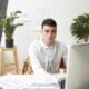 job career success concept indoor shot talented young male architect wearing white shirt sweater tied around his neck using cad program computer while working construction project