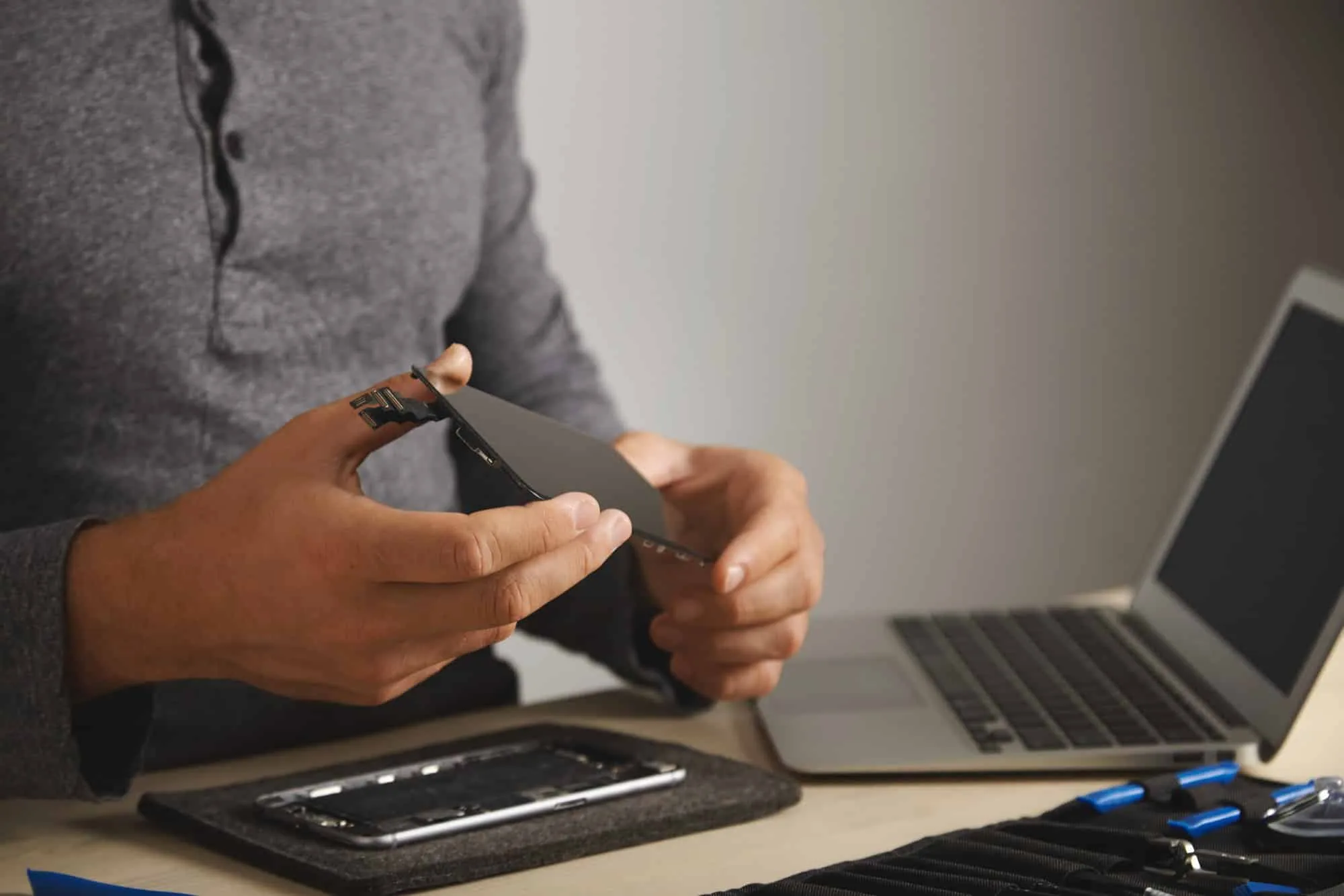 master-holds-new-screen-replacement-disassembled-smartphone-his-laboratory-tool-kit-with-instruments-laptop-front-him-white-table-close-view