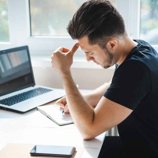 side view businessman writing something his notebook using mobile smart phone while working