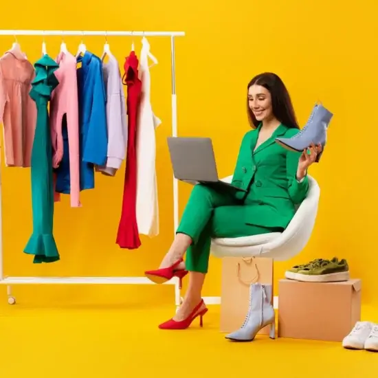 young lady shop assistant holding elegant shoe using laptop sitting near clothing rail receiving online orders jpg