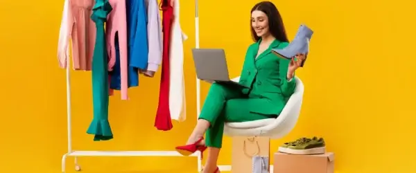 young lady shop assistant holding elegant shoe using laptop sitting near clothing rail receiving online orders jpg