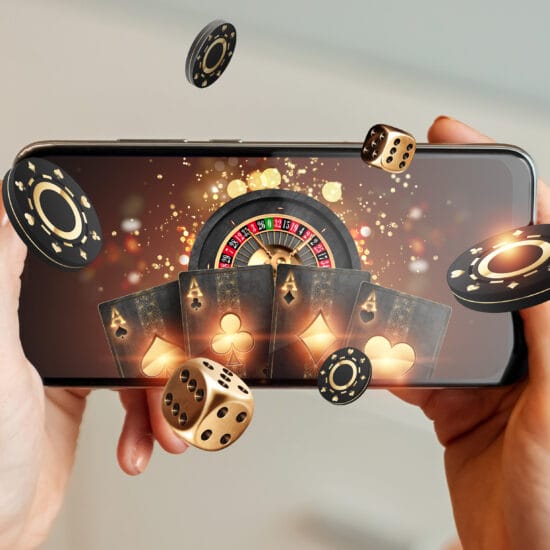 Creative background, online casino, in a man's hand a smartphone with playing cards, roulette and chips, black-gold background. Internet gambling concept. Copy space