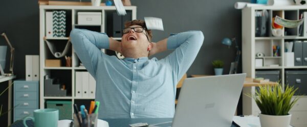lots of money falling on handsome guy in office sitting at desk alone enjoying wealth.